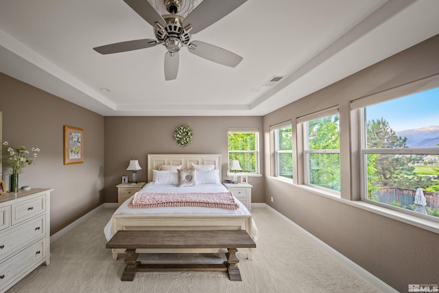 bedroom with ceiling fan, a raised ceiling, and light carpet