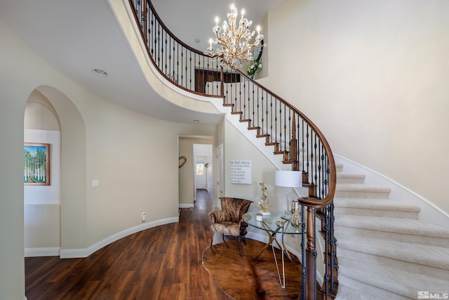 staircase with an inviting chandelier, wood-type flooring, and a high ceiling