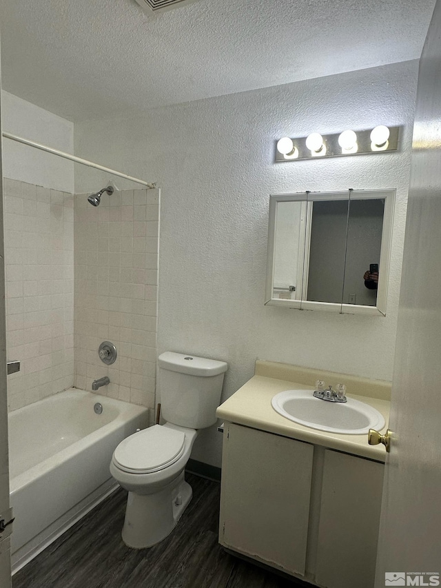 full bathroom featuring vanity, wood-type flooring, a textured ceiling, tiled shower / bath, and toilet