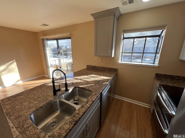 kitchen with sink, gray cabinets, stainless steel appliances, dark hardwood / wood-style floors, and dark stone counters