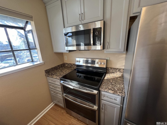 kitchen with appliances with stainless steel finishes, light hardwood / wood-style floors, and dark stone counters