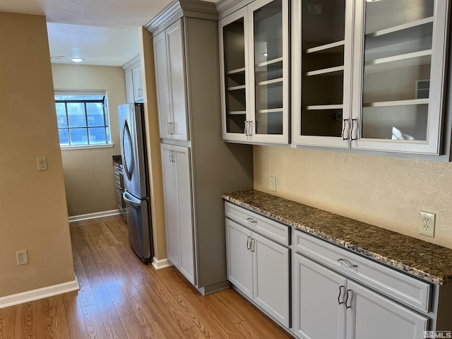 kitchen featuring white cabinets, stainless steel refrigerator, dark stone counters, and light wood-type flooring