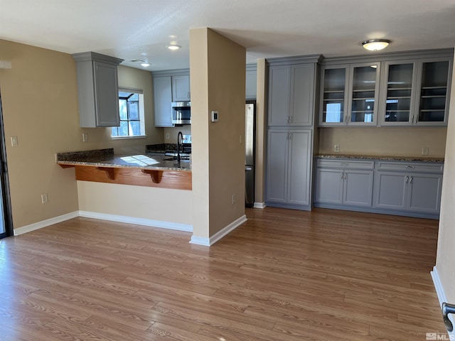 kitchen featuring sink, gray cabinets, appliances with stainless steel finishes, stone countertops, and light wood-type flooring