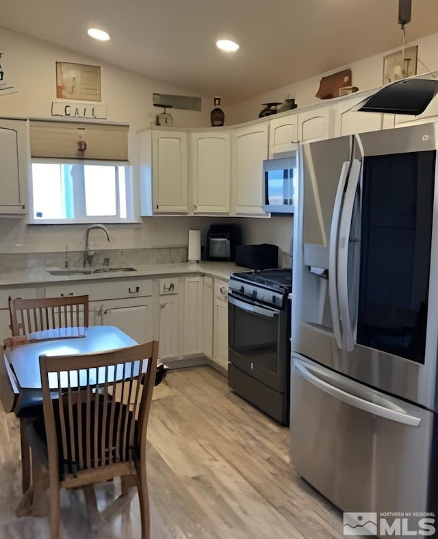 kitchen featuring white cabinetry, stainless steel refrigerator with ice dispenser, sink, and black gas range