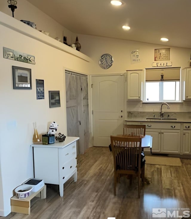 kitchen with vaulted ceiling, wood-type flooring, sink, white cabinets, and backsplash