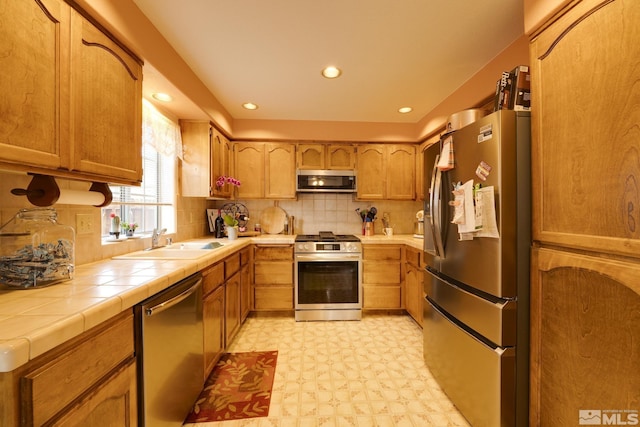 kitchen with sink, backsplash, tile countertops, and appliances with stainless steel finishes