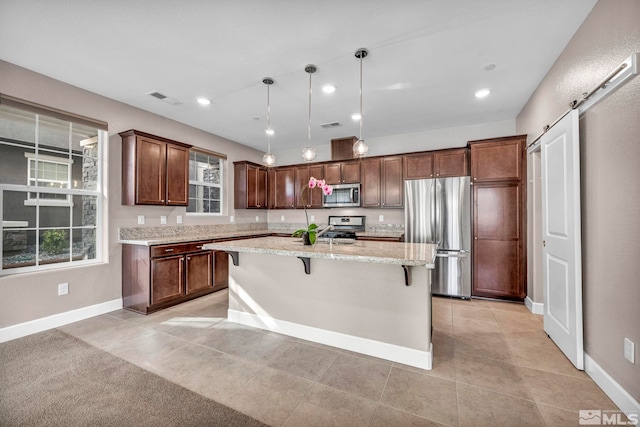 kitchen featuring appliances with stainless steel finishes, an island with sink, a kitchen bar, decorative light fixtures, and light tile patterned flooring