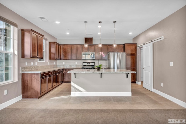 kitchen featuring appliances with stainless steel finishes, hanging light fixtures, a center island, light stone counters, and a barn door