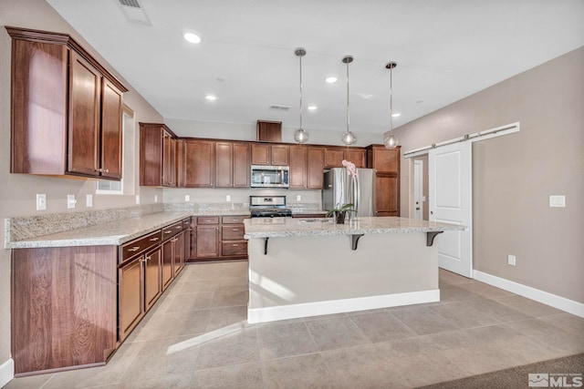 kitchen with light stone counters, decorative light fixtures, a center island with sink, stainless steel appliances, and a barn door