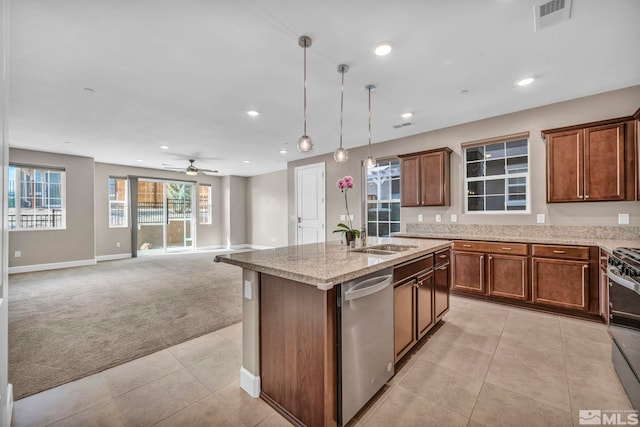 kitchen with sink, appliances with stainless steel finishes, a kitchen island with sink, hanging light fixtures, and light colored carpet