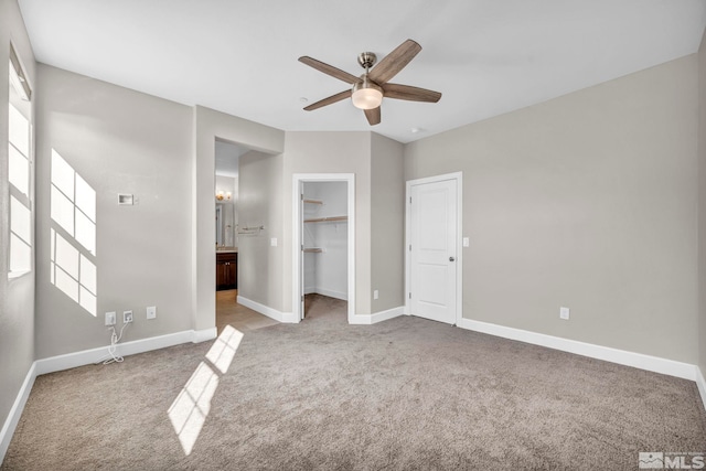 unfurnished bedroom featuring ceiling fan, a walk in closet, a closet, and light carpet