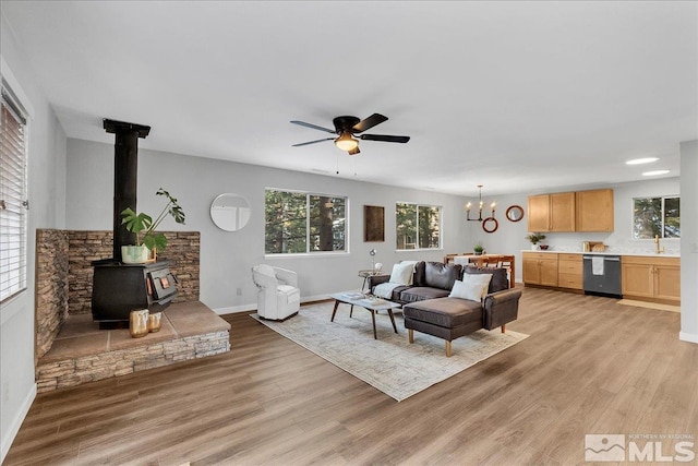 living room featuring sink, ceiling fan with notable chandelier, light hardwood / wood-style flooring, and a wood stove