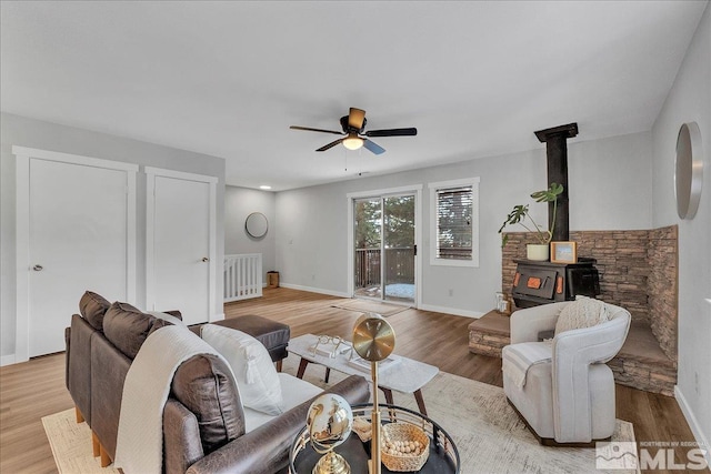 living room featuring ceiling fan, light hardwood / wood-style floors, and a wood stove