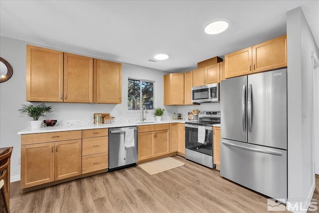 kitchen with stainless steel appliances, sink, light brown cabinetry, and light hardwood / wood-style flooring