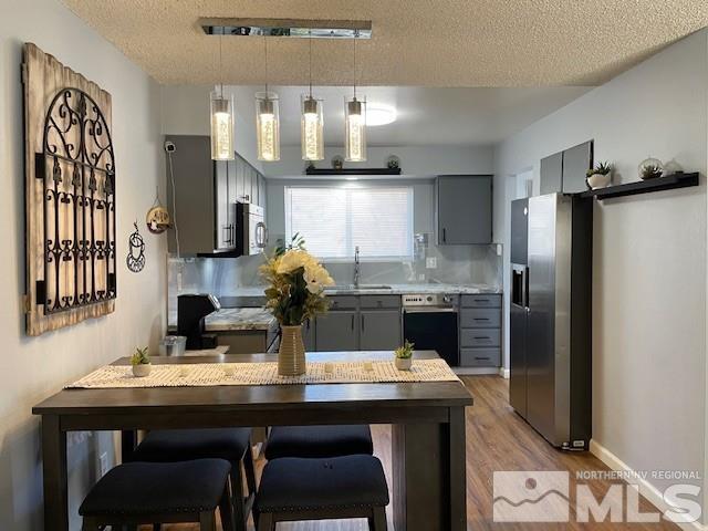 kitchen with hanging light fixtures, stainless steel appliances, light hardwood / wood-style floors, gray cabinets, and sink