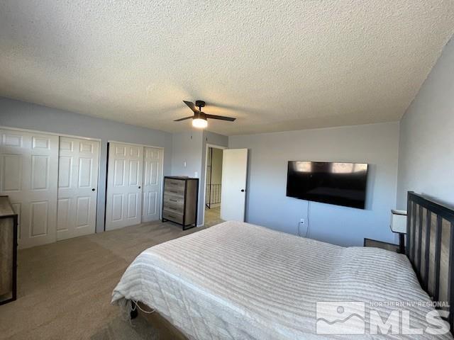 bedroom featuring light carpet, ceiling fan, multiple closets, and a textured ceiling