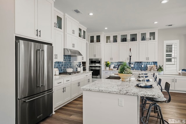 kitchen with appliances with stainless steel finishes, a breakfast bar, white cabinets, a center island, and light stone countertops