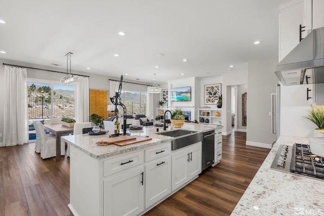 kitchen featuring decorative light fixtures, white cabinetry, an island with sink, sink, and light stone counters