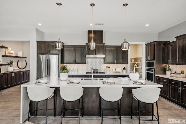 kitchen with decorative light fixtures, an island with sink, and appliances with stainless steel finishes