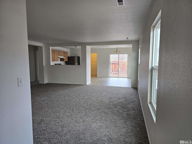 unfurnished living room with a chandelier, a textured ceiling, and carpet flooring