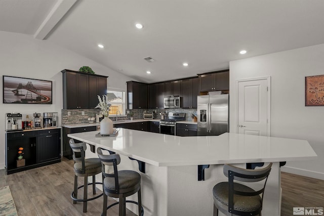 kitchen featuring a spacious island, vaulted ceiling with beams, tasteful backsplash, appliances with stainless steel finishes, and a kitchen breakfast bar