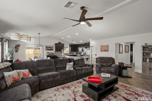 living room with vaulted ceiling, ceiling fan with notable chandelier, and light hardwood / wood-style floors