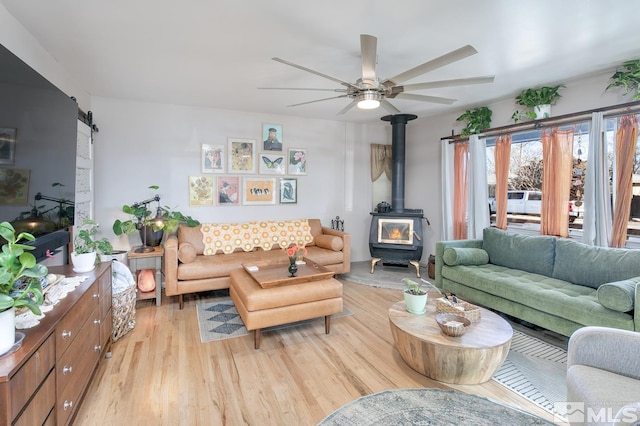 living room featuring ceiling fan, a barn door, a wood stove, and light wood-type flooring