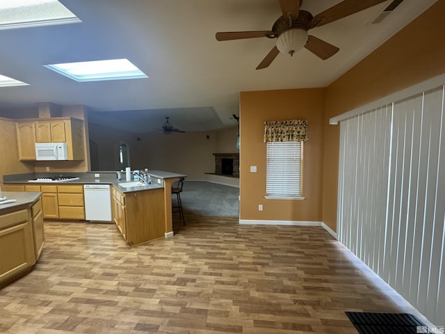 kitchen featuring sink, white appliances, a breakfast bar, light brown cabinets, and light wood-type flooring