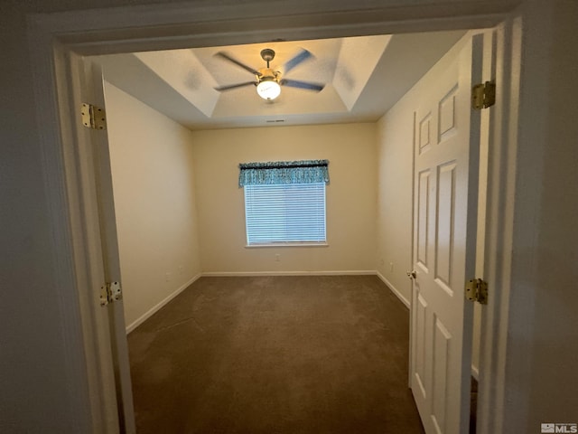 unfurnished room featuring dark carpet, a raised ceiling, and ceiling fan