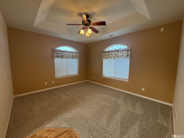 carpeted spare room with a tray ceiling and ceiling fan