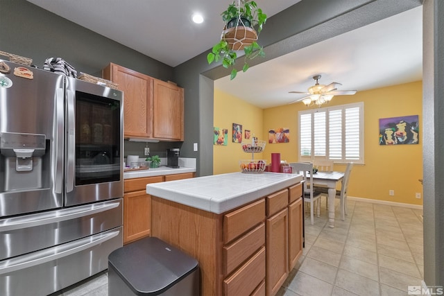 kitchen featuring light tile patterned floors, stainless steel fridge, ceiling fan, a kitchen island, and tile countertops