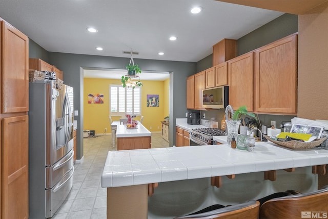 kitchen with stainless steel appliances, a breakfast bar area, tile countertops, and kitchen peninsula