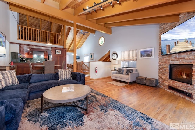 living room with a stone fireplace, hardwood / wood-style flooring, ceiling fan, wood ceiling, and beam ceiling