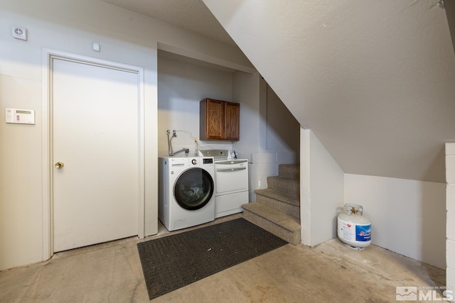 clothes washing area with separate washer and dryer and cabinets