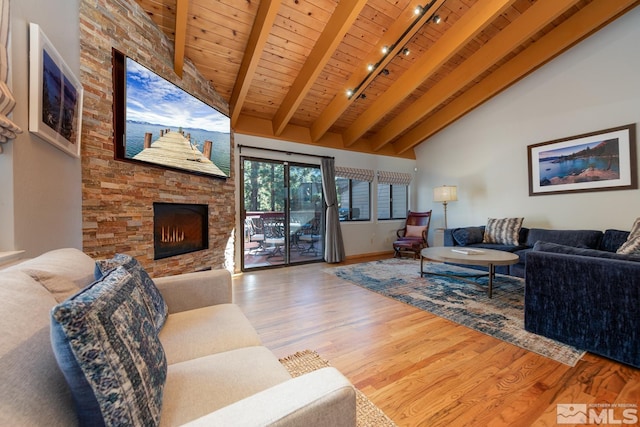 living room featuring wood ceiling, hardwood / wood-style flooring, rail lighting, a stone fireplace, and beamed ceiling