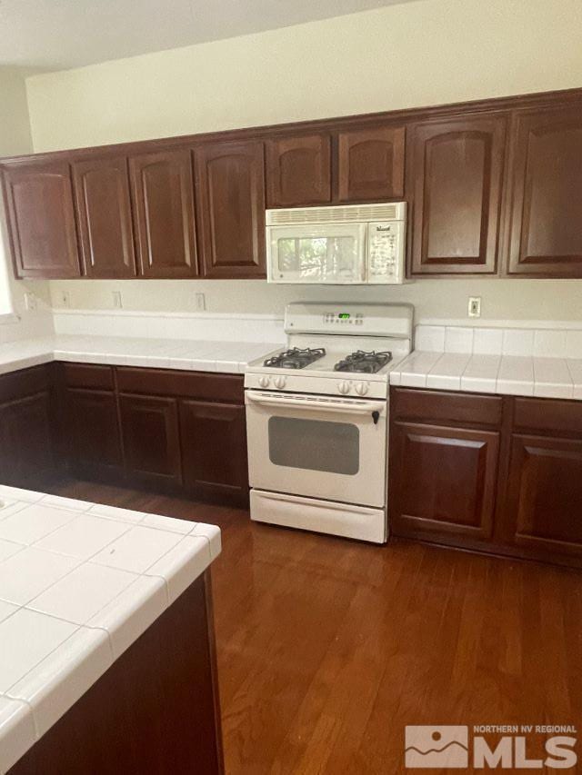 kitchen with white appliances, dark brown cabinetry, tile counters, and dark hardwood / wood-style flooring