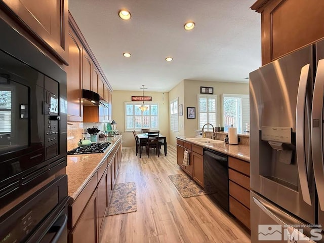 kitchen featuring sink, hanging light fixtures, light stone counters, black appliances, and light hardwood / wood-style flooring