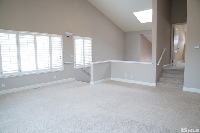 carpeted empty room with a skylight and high vaulted ceiling