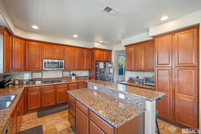 kitchen with a kitchen island, appliances with stainless steel finishes, sink, a kitchen breakfast bar, and light stone countertops