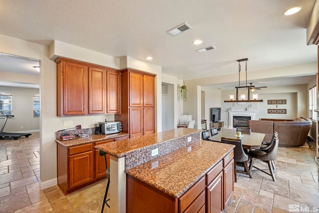 kitchen with light stone counters, a center island, a textured ceiling, a kitchen breakfast bar, and pendant lighting