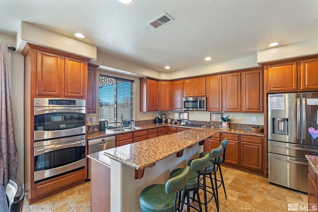 kitchen featuring sink, a breakfast bar area, appliances with stainless steel finishes, light stone countertops, and a kitchen island