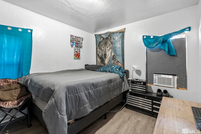 bedroom with cooling unit, a textured ceiling, and light wood-type flooring