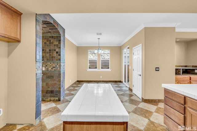 kitchen featuring tile countertops, a chandelier, a center island, decorative light fixtures, and ornamental molding