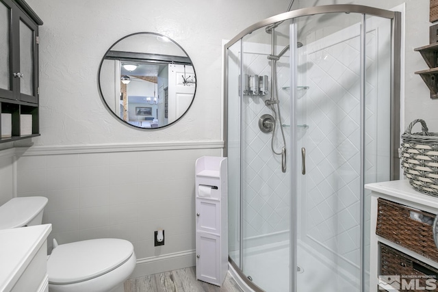 bathroom with a shower with door, vanity, tile walls, and toilet