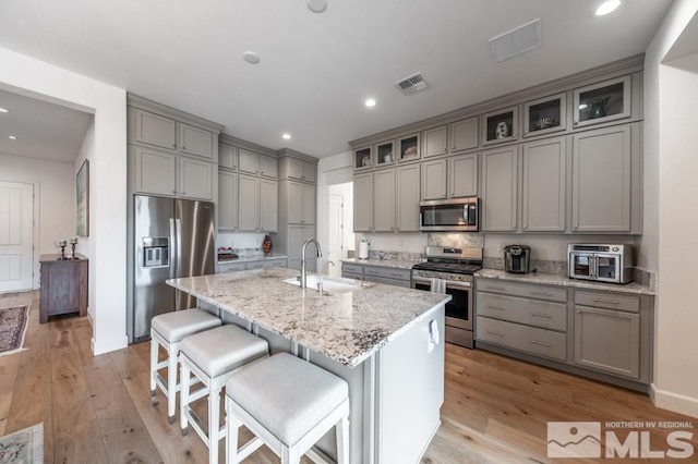 kitchen featuring a breakfast bar, sink, light stone counters, appliances with stainless steel finishes, and a kitchen island with sink