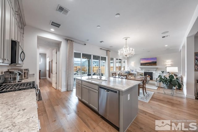 kitchen featuring sink, gray cabinetry, stainless steel appliances, light stone countertops, and a center island with sink