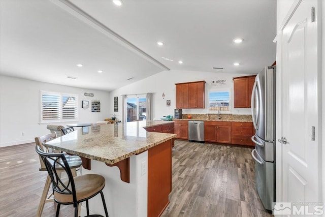 kitchen with a kitchen island, appliances with stainless steel finishes, a kitchen breakfast bar, hardwood / wood-style flooring, and light stone counters