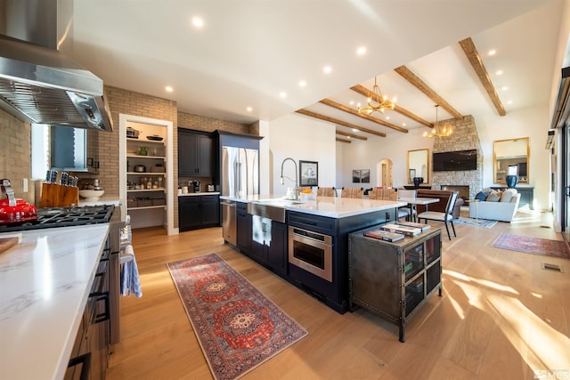 kitchen featuring brick wall, appliances with stainless steel finishes, island range hood, an island with sink, and sink