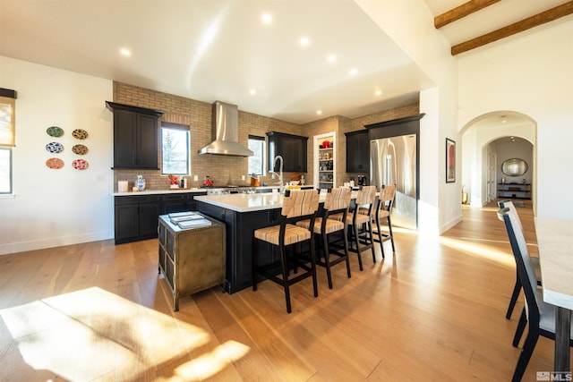 kitchen featuring high end fridge, a breakfast bar area, light hardwood / wood-style flooring, an island with sink, and wall chimney range hood