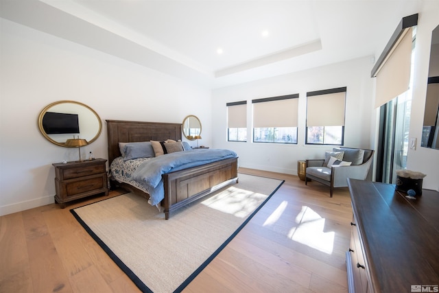 bedroom with a raised ceiling and light wood-type flooring